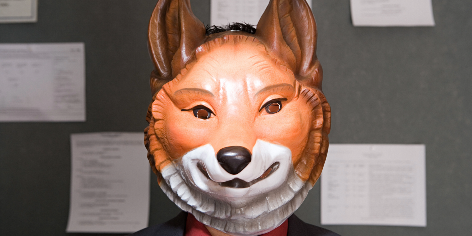 Person in a business suit wearing a fox mask, symbolizing cunning, strategy, and the act of playing dumb while secretly outsmarting others.