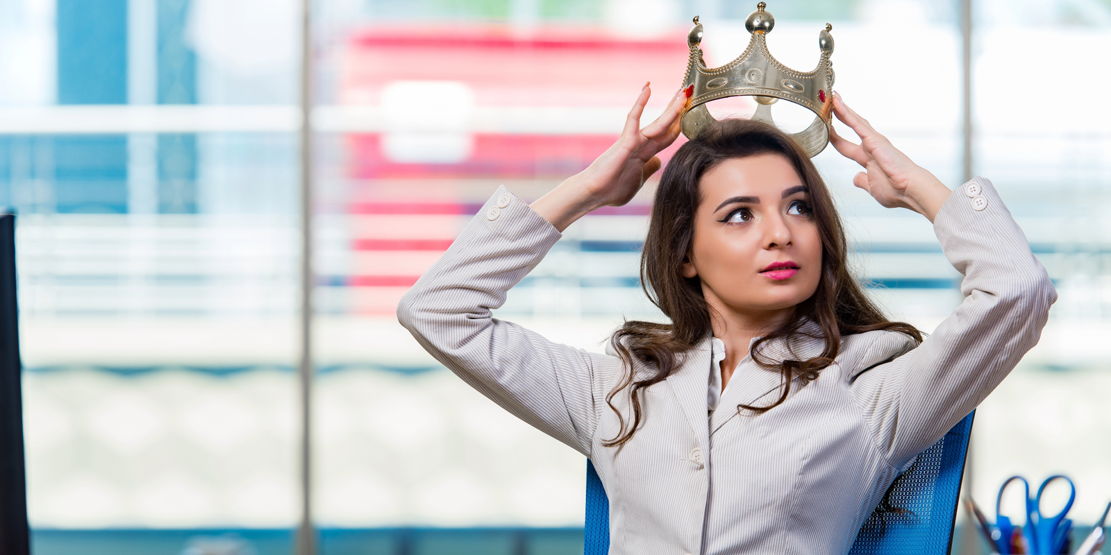 Businesswoman in an office carefully placing a gold crown on her head, symbolizing unexpected success and promotion through unconventional strategy.